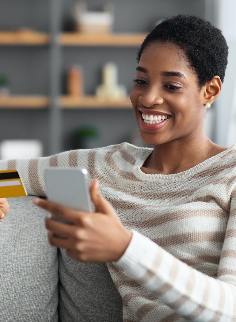 Smiling woman in striped sweater using smartphone while holding a credit card.